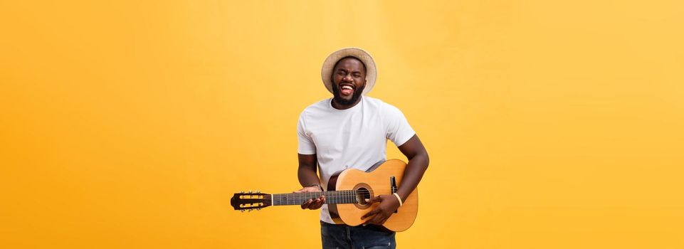 Handsome african american retro styled guitarist playing acoustic guitar isolated on yellow background