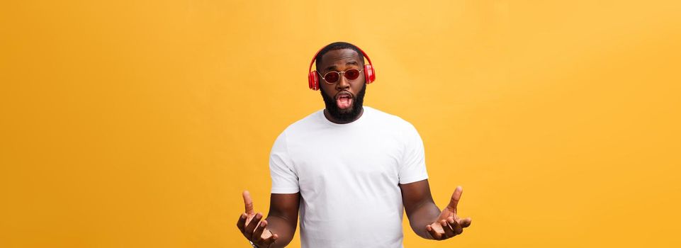 Young African American man wearing headphone and enjoy music over yellow gold Background.