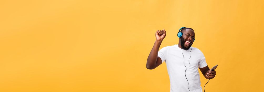 African American man with headphones listen and dance with music. Isolated on yellow background.