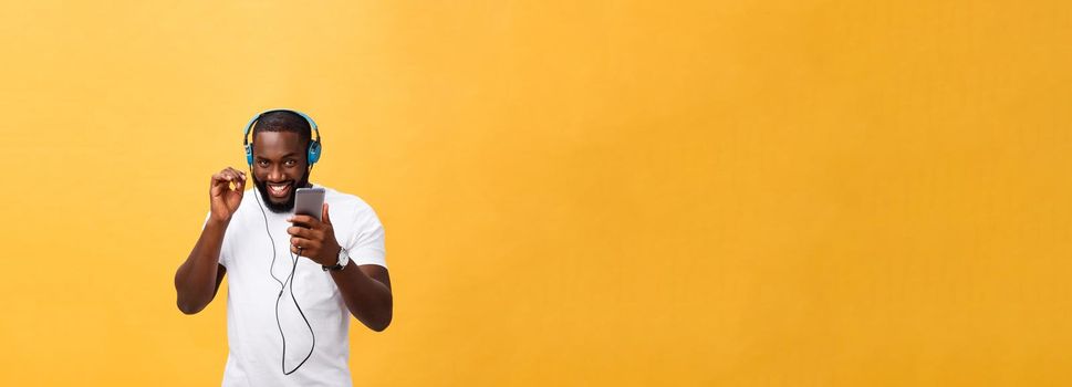 African American man with headphones listen and dance with music. Isolated on yellow background.