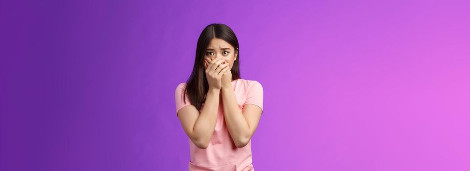 Shocked female asian victim frightened, gasping witness crime, close mouth hands, frowning, stare camera scared upset, make innocent terrified gaze, stand purple background. Copy space