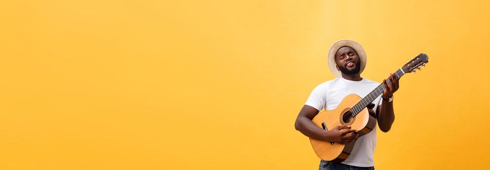 Muscular black man playing guitar, wearing jeans and white tank-top. Isolate over yellow background