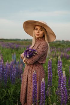 A beautiful woman in a straw hat walks in a field with purple flowers. A walk in nature in the lupin field.
