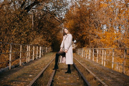 A beautiful long-haired woman walks through the autumn streets. Railway, autumn leaves, a woman in a light coat.