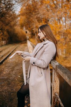 A beautiful long-haired woman walks through the autumn streets. Railway, autumn leaves, a woman in a light coat.