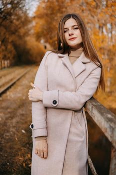 A beautiful long-haired woman walks through the autumn streets. Railway, autumn leaves, a woman in a light coat.