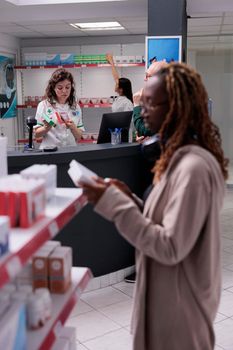 Pharmacy customers doing pharmaceutical shopping, buying vitamin, supplements for immune system. Elderly client discussing with drugstore worker asking for help with drugs prescription,