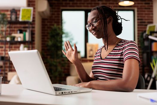 Smiling young freelancer greeting client on videocall interview, woman working on laptop in home office. Employee attending virtual meeting, looking at computer camera, waving hi