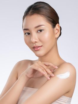 Gorgeous girl with soft makeup applying moisturizing skincare cream on shoulder isolated over white background. Skincare cream applied by female model concept.