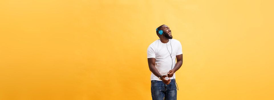Full length portrait of a cherry young african american man listening to music with headphones and dancing isolated over yellow background.