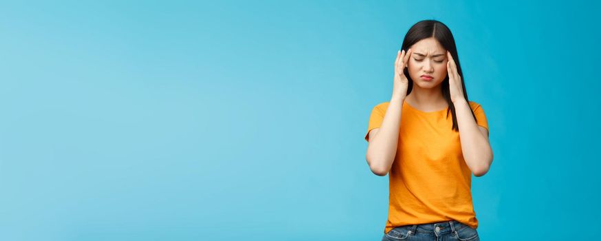 Distressed tired asian woman dark haircut cringe touch temples, suffer huge migraine need painkillers, painful headache, feel dizzy, stand blue background intense drained. Copy space