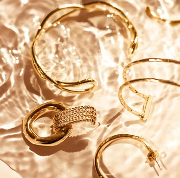 Jewellery branding, fashion gift and luxe shopping concept - Golden bracelets, earrings, rings, jewelery on gold water background, luxury glamour and holiday beauty design for jewelry brand ads