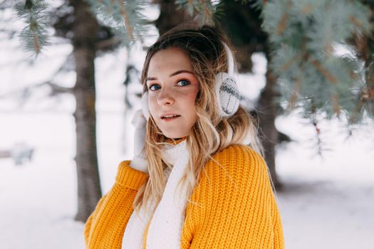 Teen blonde in a yellow sweater outside in winter. A teenage girl on a walk in winter clothes in a snowy forest.