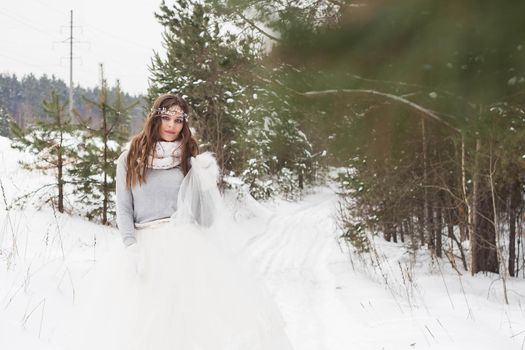 Beautiful bride in a white dress with a bouquet in a snow-covered winter forest. Portrait of the bride in nature.