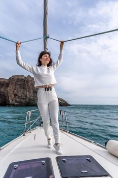 Woman standing on the nose of the yacht at a sunny summer day, breeze developing hair, beautiful sea on background.