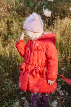 A little girl in a red coat walks in nature in an autumn grove. The season is autumn.