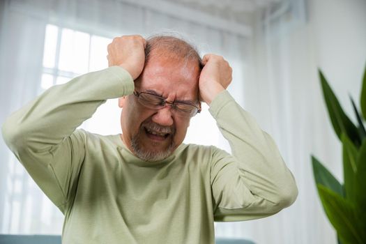 Headache. Close up of elderly holds head with hand suffering from migraine headache, Sad Asian senior man sitting on sofa feeling hurt and lonely at home, Old age health problems, healthcare