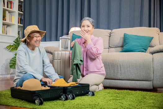 Asian couple old senior marry retired prepare luggage suitcase arranging for travel, Romantic retired couple packing clothes travel bag suitcase together on floor at home interior living room