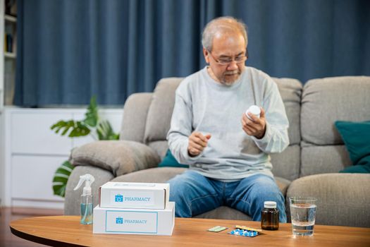 Asian worried senior man with medicine pills to taking on table in the living room, old man buy herbal self cure Rx pill online from pharmacy, home isolation, health care help service