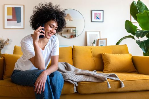 Happy African American woman on mobile phone call sitting at home couch. Copy space. Lifestyle concept.