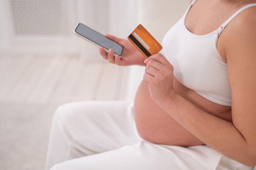 A pregnant woman is holding a smartphone and a credit card. Online shopping concept