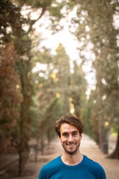 Happy young caucasian man standing in the forest looking at camera. Copy space. Vertical. Path of life concept.