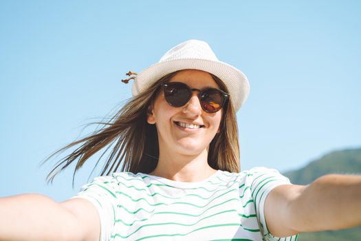 Woman taking selfie photo with wide angle front camera of mountains lake background. Traveler female having fun on the blue lake outdoors travel adventure vacation.