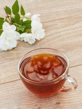 Glass cup of tea with white jasmine flowers on wooden background. Top view.