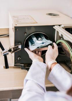 Close up of hands with dental autoclave sterilizer machine. Dentist hands sterilizing tools with autoclave, dentist with dental autoclave, close up of dentist with steam sterilizer