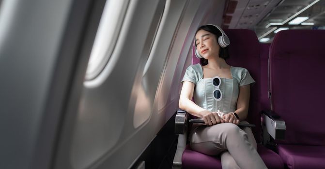 Joyful asian woman sits in the airplane and listen music while go to travel.