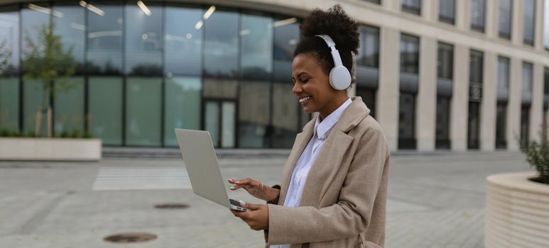 young African American woman cybersecurity specialist with a laptop in her hands and headphones on the background of the office center.