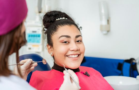 Smiling patient in dentist's chair, Professional dentist examining female patient in office. Close up of smiling patient at dentist's office looking at camera