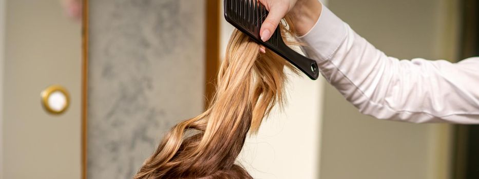 Professional hair care. Young female blonde with long hair receiving hairstyling in a beauty salon