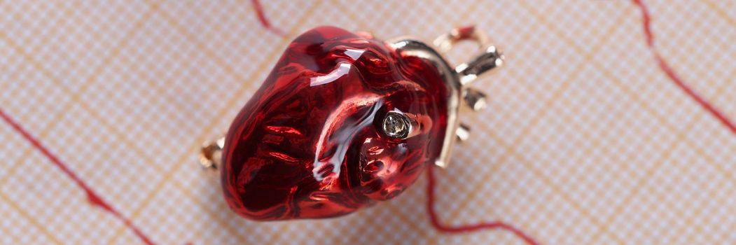 Top view of red glass miniature heart placed over heart cardiogram result paper. Examination of cardiovascular system. Medicine, cardiology, health concept