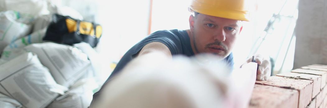 Portrait of concentrated male builder measure distance with level equipment. Big concrete wall made of red bricks. Renovation, construction site concept