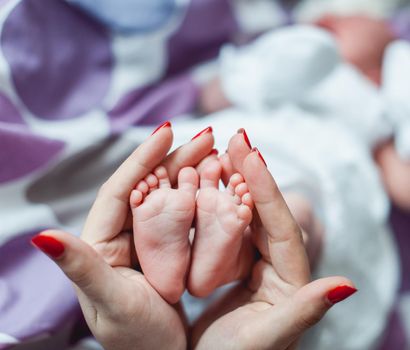 Baby feet in mother and father hands. Tiny Newborn Baby's feet on female Heart Shaped hands closeup. Mom, dad and their Child. Happy Family concept. Beautiful conceptual image of Maternity