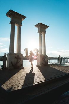 Happy teenage party girl 12-13 years old with balloons. Standing on the lake side between columns. look from the back. silhouette