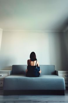 Loneliness. Alienation. Girl in an empty room sits back on a couch and stares in the wall