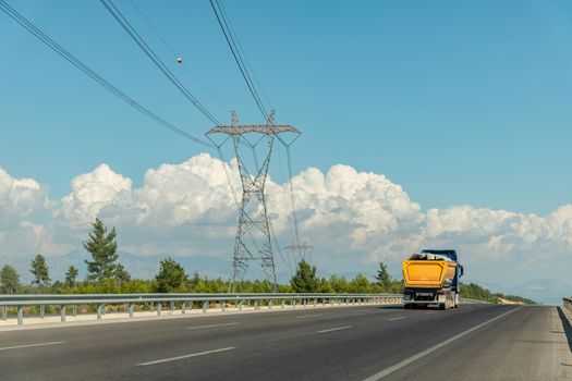 A truck going on a highway and a high-voltage power line on the side of the highway