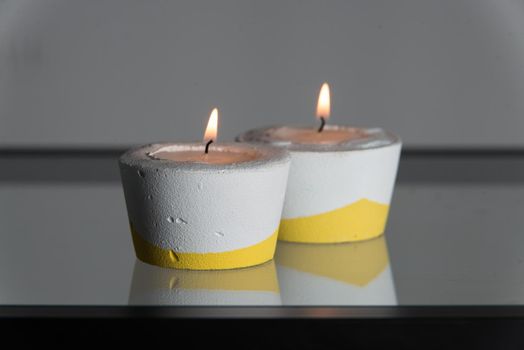 Two candles in white and yellow concrete candle holders.