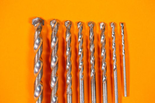 Drills for metal of different sizes for a drill on an orange background. Building tool