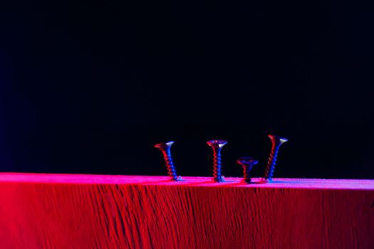 Screws screwed into a wooden beam in hard red light