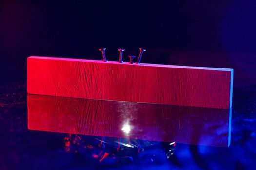 Screws screwed into a wooden beam in hard red light