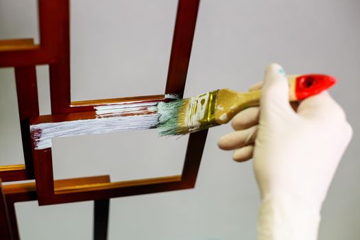 the master paints with a brush a wooden brown photo frame with light paint