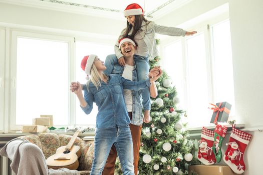 Family decorating a Christmas tree. Young man with his daughter on his shoulders helping her decorate the Christmas tree.