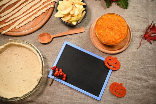 Empty blackboard with copy advertising space for insert promotional text on a linen tablecloth, next to fresh ingredients and homemade American classic pumpkin and apple pie, for Thanksgiving dinner