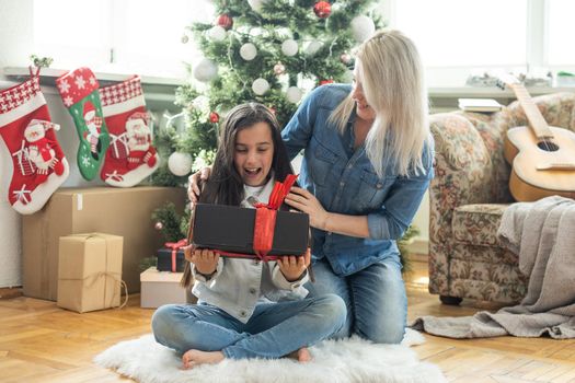 Mother with her child daughter celebrating near Christmas tree.