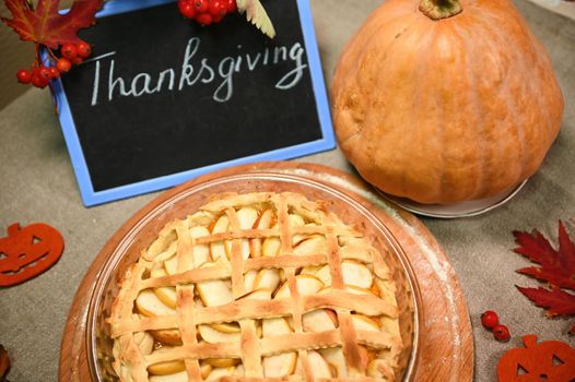 Selective focus. Top view. Branch of viburnum berries hanging on a blackboard with lettering Thanksgiving Day, autumn maple leaves, sweet homemade classic American pumpkin apple pie with crispy crust