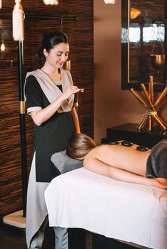 Specialist making biolocation with crystal pendulum. Young charming girl on a panchakarma procedure laying on a massage table. beautiful woman spending time at modern spa cabinet relaxing. Soft yellow light.