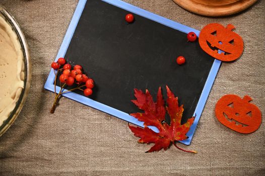 Empty chalk board with copy advertising space for insert promotional text on a linen tablecloth, next to viburnum berries and maple leaves. Autumn holidays concept. Thanksgiving Day and Halloween